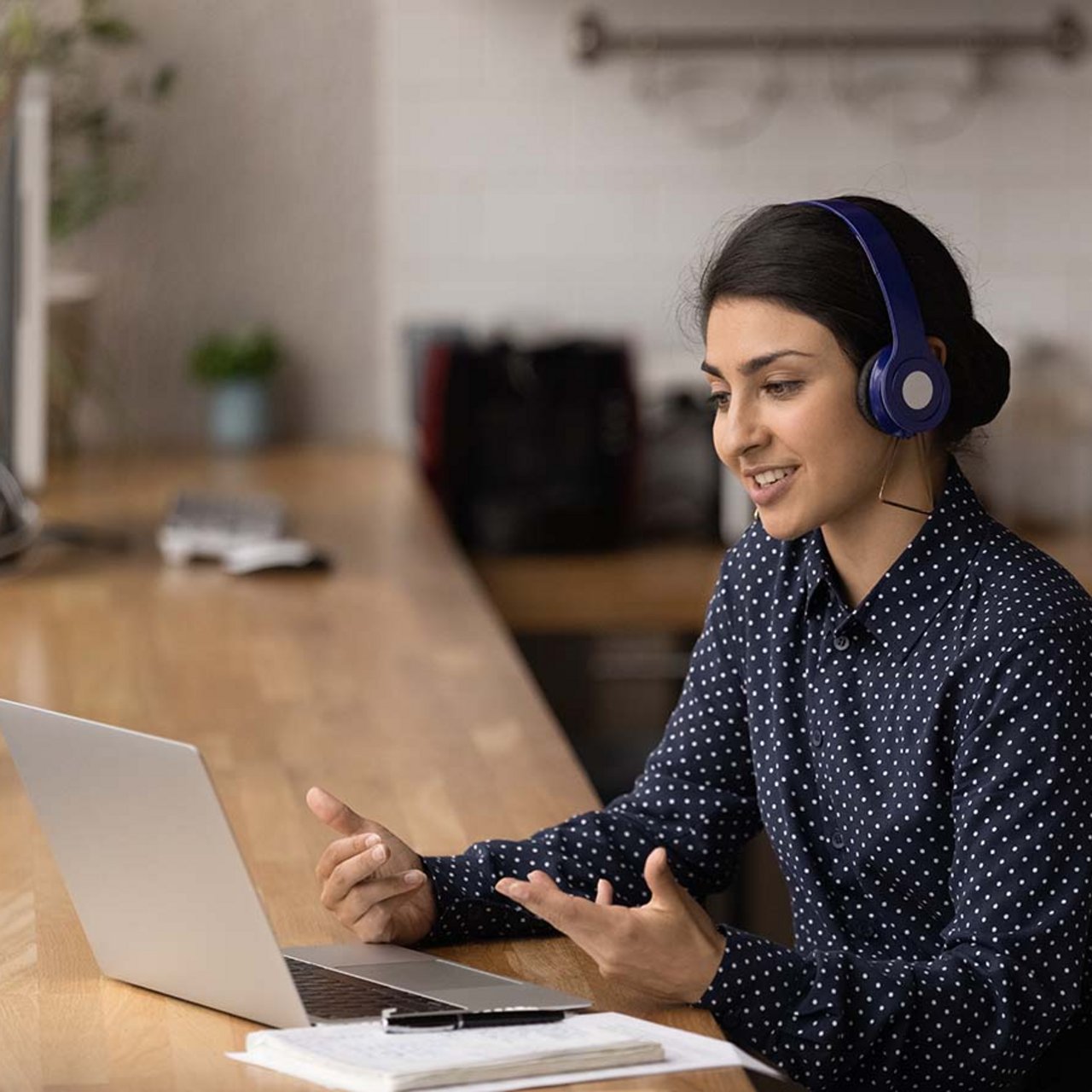 Junge Dolmetscherin mit Migrationshintergrund sitzt am Laptop mit Headset und führt eine Live-Übersetzung per Video durch.