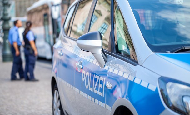 Polizeiauto von der Seite mit Polizisten im Hintergrund