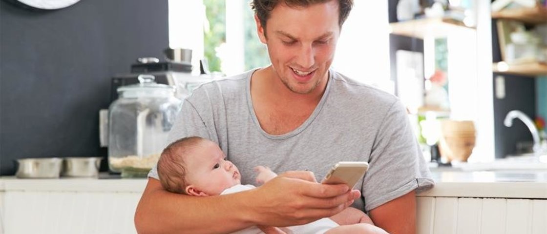 Mann mit Baby im Arm und schaut auf ein Handy