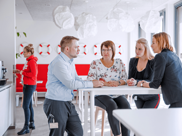 In der Schulungspause stehen Menschen an einem Stehtisch und reden miteinander