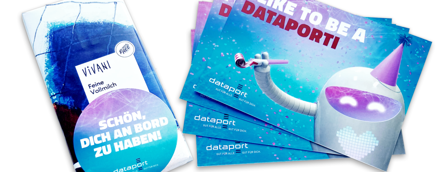 Zu sehen ist das Willkommenspaket bestehend aus einer Tafel Schokolade und einer Karte auf der das Maskotten Porti abgebildet ist, mit dem Satz I LIKE TO BE A DATAPORTI.