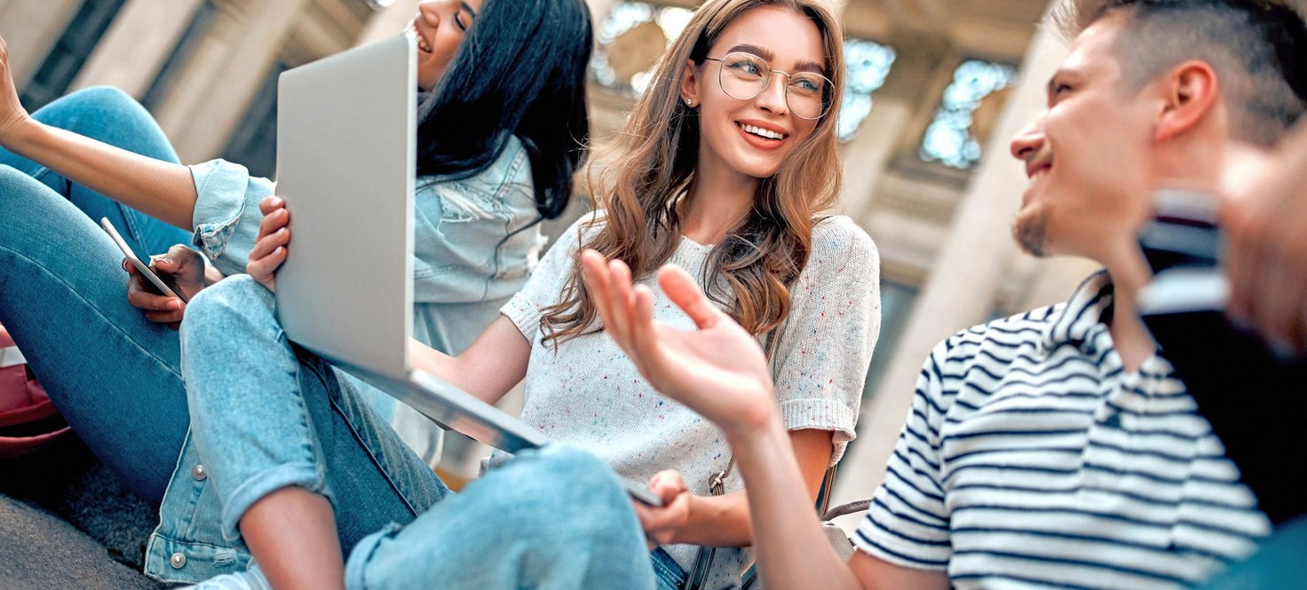 Junge Menschen sitzen mit ihren Notebooks draußen vor einem Gebäude
