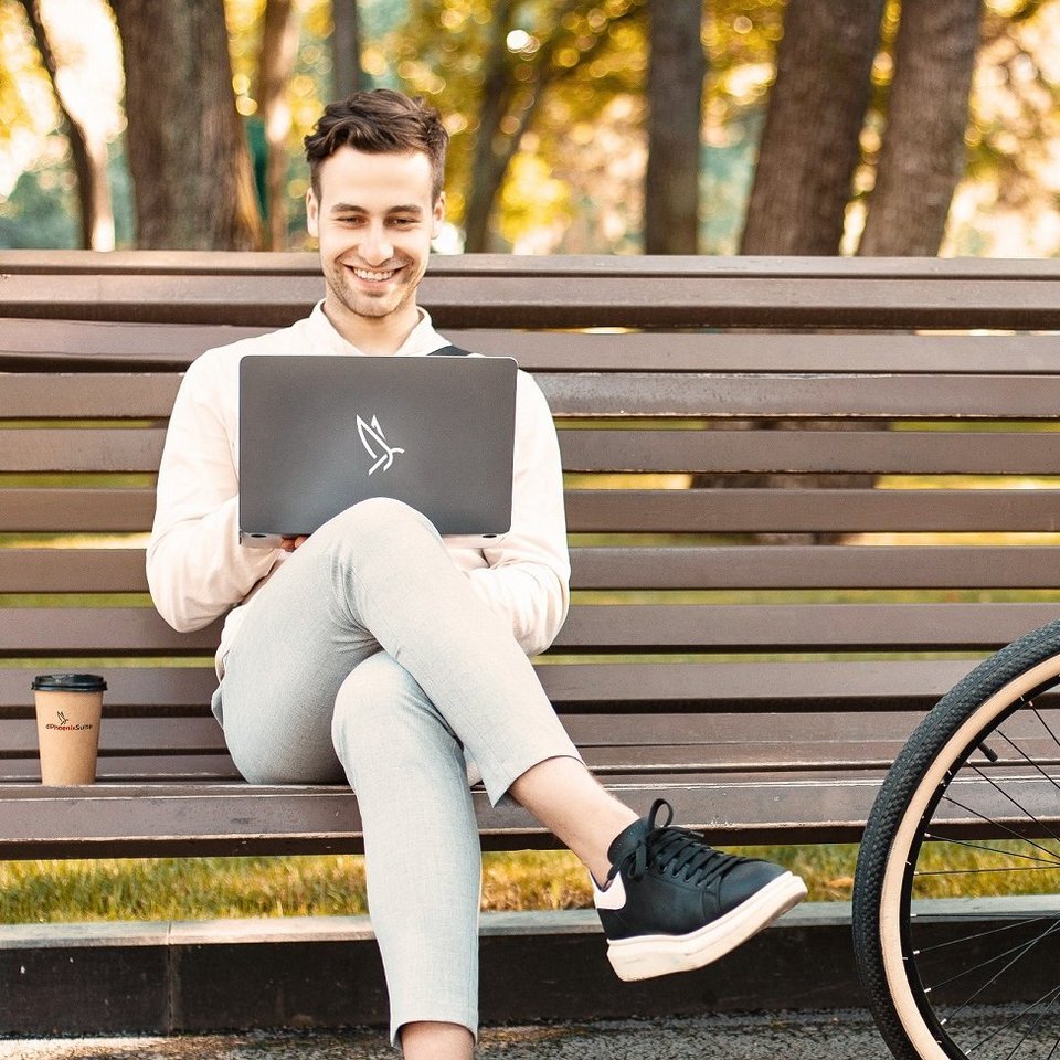 Man sitting in a park with a laptop on his knees and smiles while working