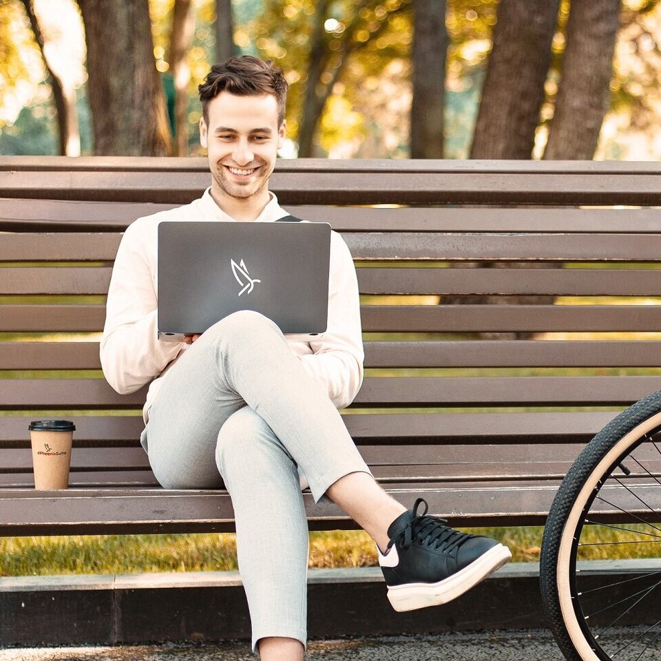 Mann mit Laptop und Coffee-To-Go auf Parkbank