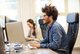 Zwei Menschen sitzen in ihrem Büro am Computer und lächeln.