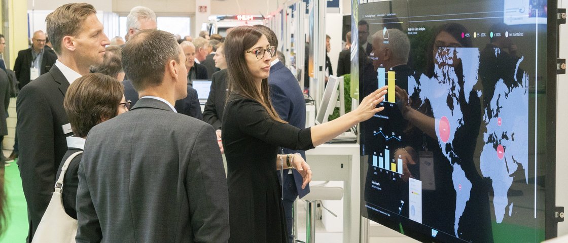 Besucher der Hausmesse stehen vor einem interaktivem Bildschirm