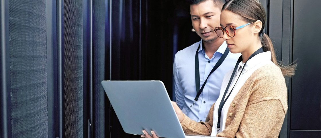 Eine Frau und ein Mann arbeiten im Serverraum an einem Notebook
