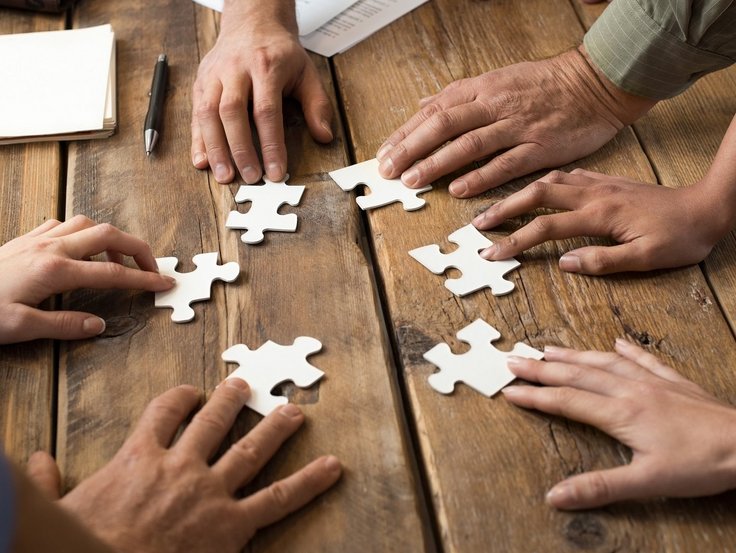 Hände verschiedener Teilnehmer puzzlen am Tisch