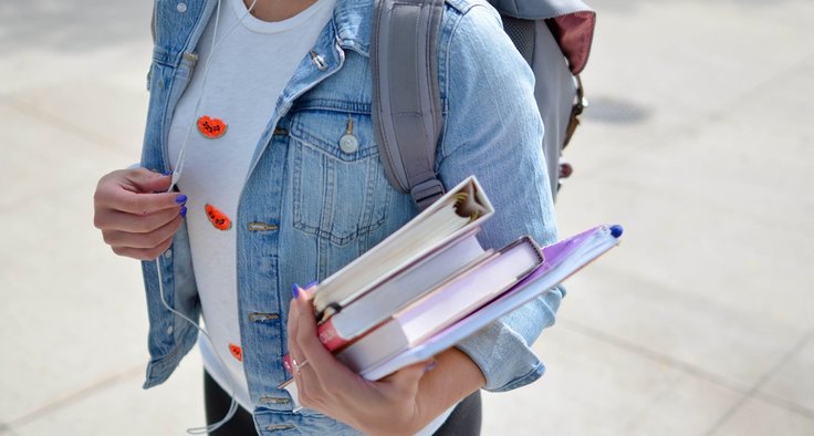 Schülerin mit einem Stapel Bücher auf dem Arm