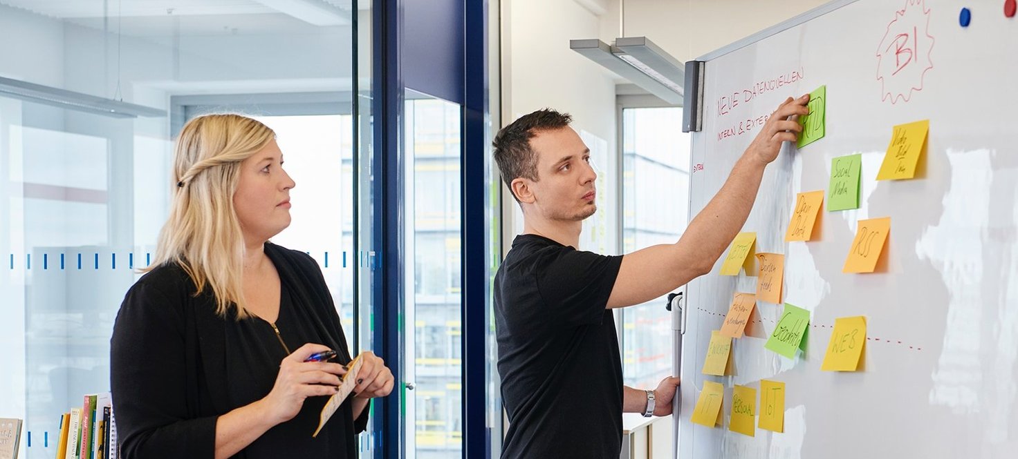 Zwei Personen vor einem Whiteboard mit Post-Its darauf