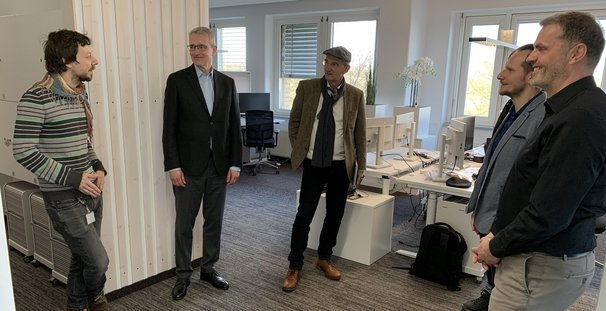 Christian Pfromm und Dr. Johann Bizer unterhalten sich im Kreis stehend mit Kollegen in den Räumlichkeiten in Halle.