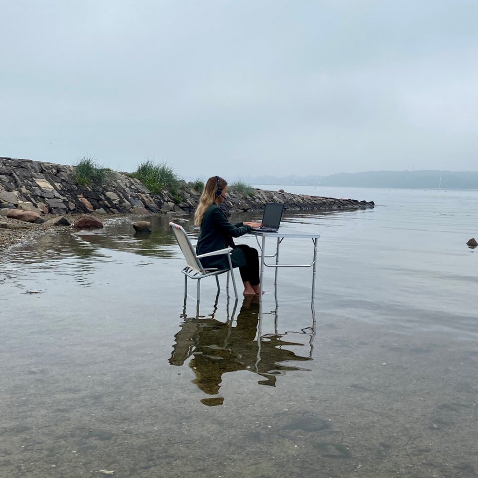 Frau sitzt mit Laptop und Headset am Campingtisch am Meer