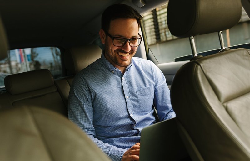 Ein Mann auf der Rückbank eines Autos sieht aufs Notebook