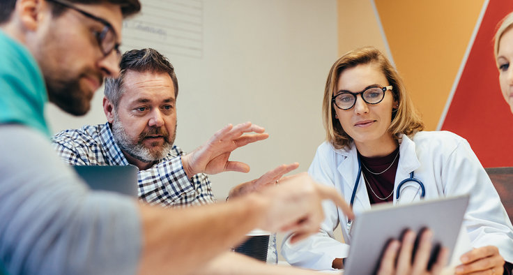 Menschen diskutieren an einem Tablet Gesundheitsthemen