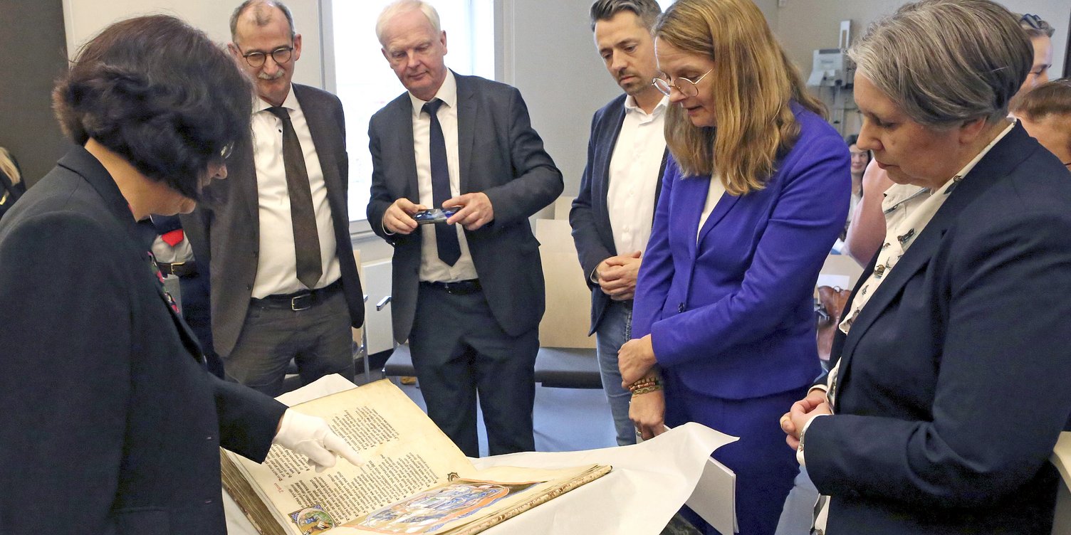 Länderübergreifende Digitalisierung: Archivinformationssystem Arcinsys jetzt auch in Mecklenburg-Vorpommern im Einsatz Personengruppe begutachtet historisches Buch im Landesarchiv in Schwerin