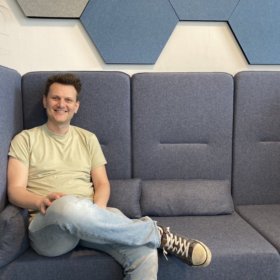 IT-Architekt Fabian Lange sitzt auf dem Sofa und lächelt freundlich in die Kamera.