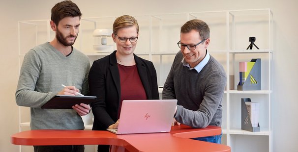 Drei Personen blicken auf Laptop und tauschen sich aus