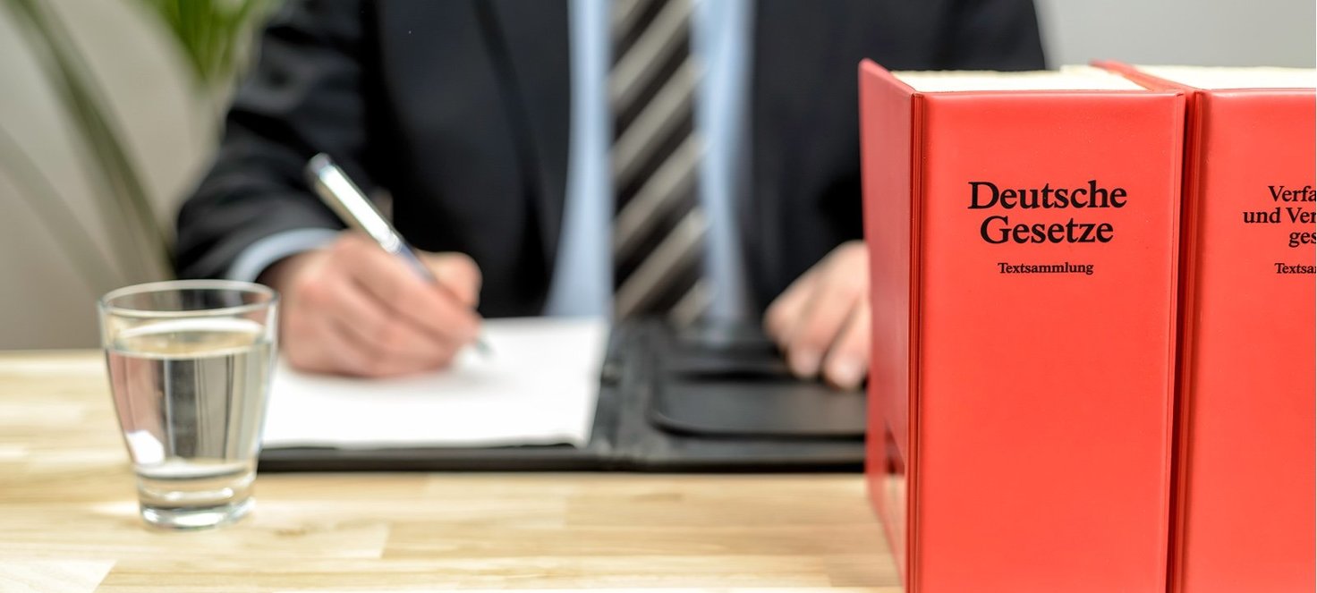 Mann mit Hemd und Krawatte am Schreibtisch mit deutschem Gesetzbuch