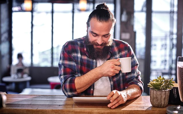 Digitale Souveränität Ein Mann mit Dutt trinkt Kaffee und sieht aufs Tablet