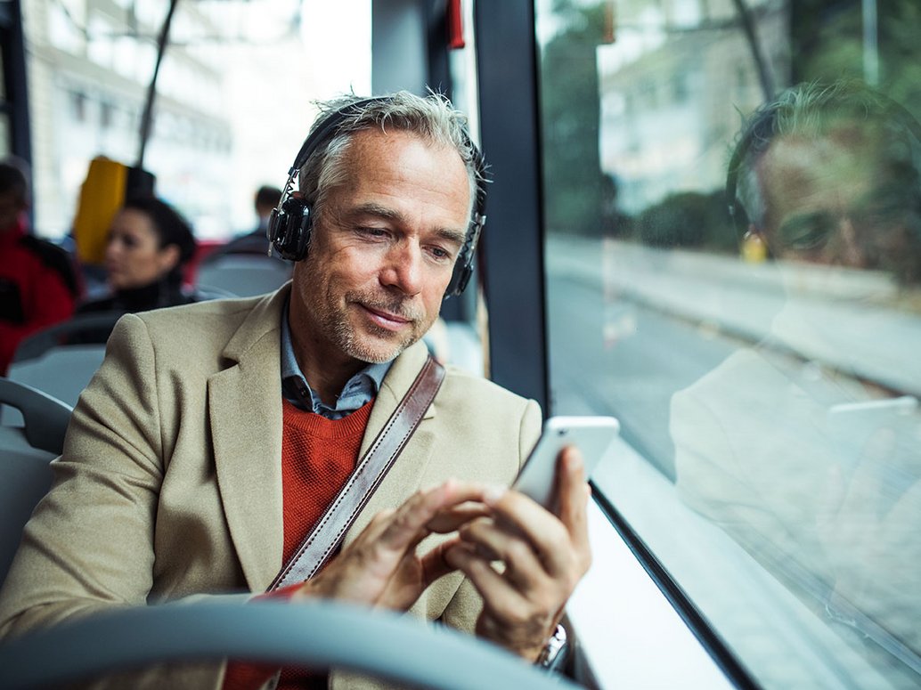Geschäftsmann mit Kopfhörern und Smartphone in der Hand fährt Bus