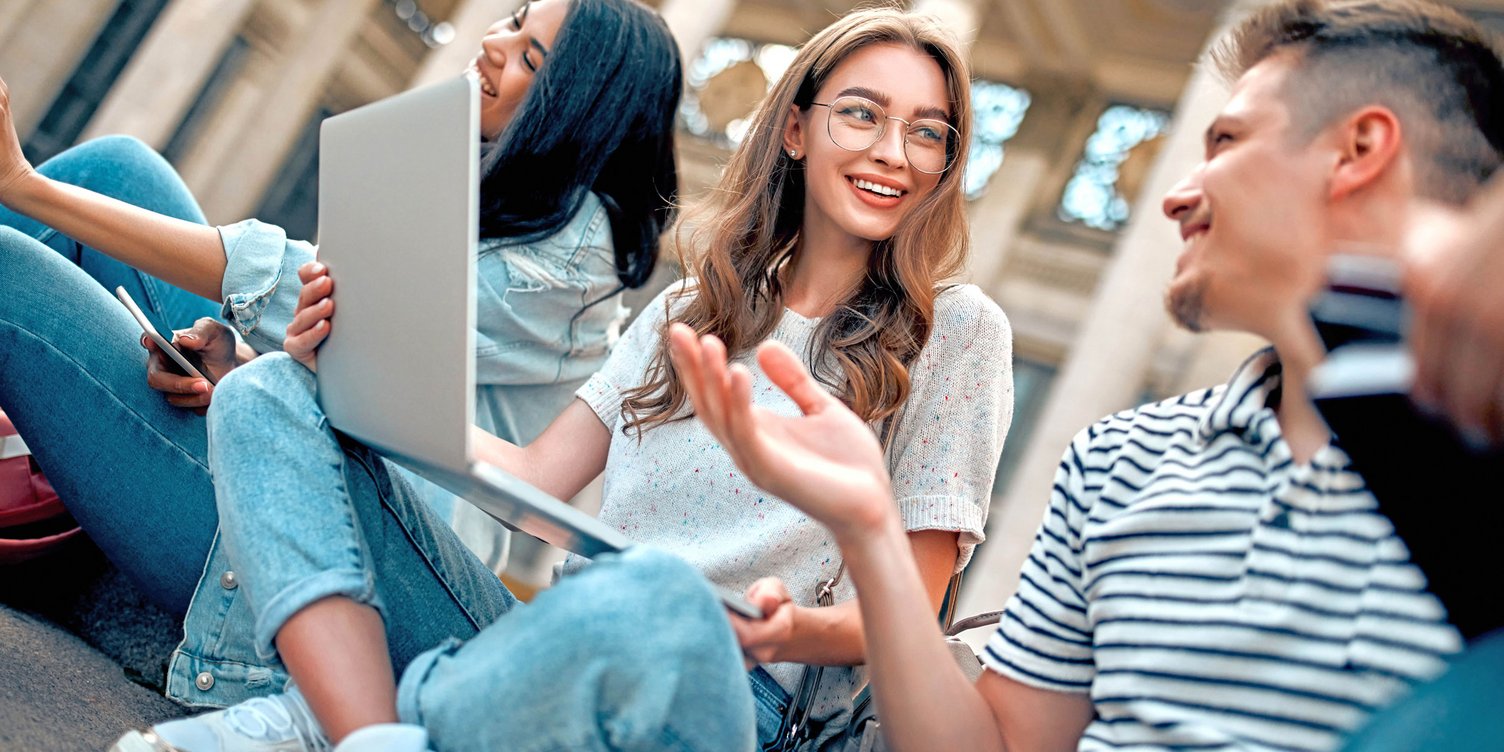 Junge Menschen sitzen mit ihren Notebooks draußen vor einem Gebäude