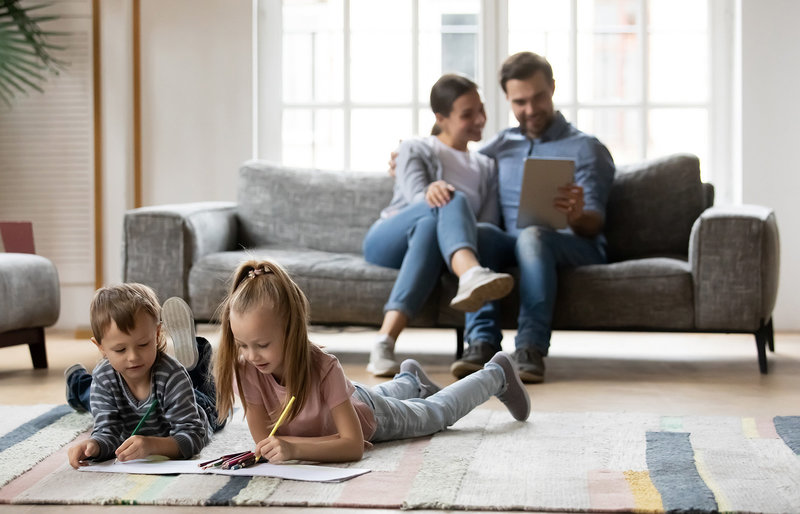 Familie im Wohnzimmer, Kinder auf dem Fußboden mit Block und Stift, Eltern mit Tablet