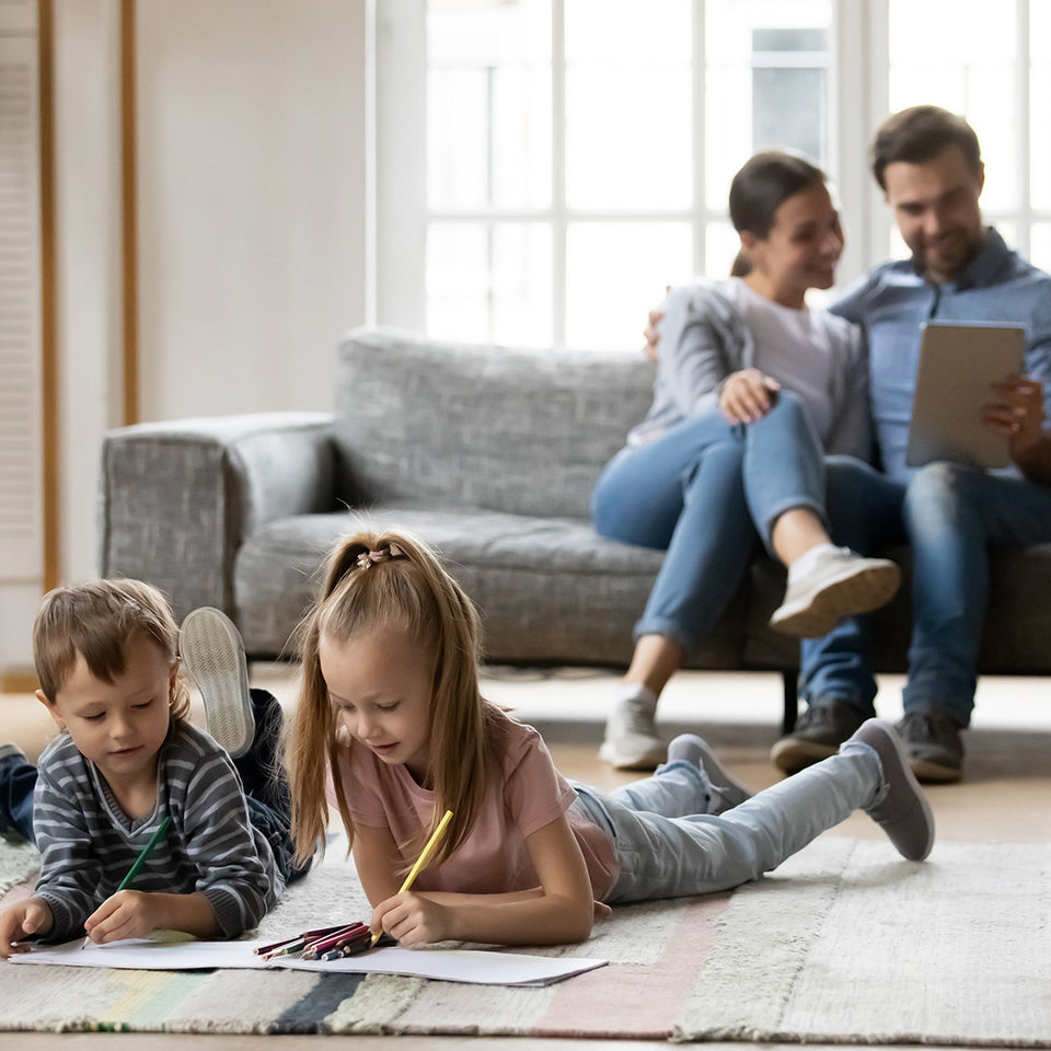 Familie im Wohnzimmer, Kinder auf dem Fußboden mit Block und Stift, Eltern mit Tablet