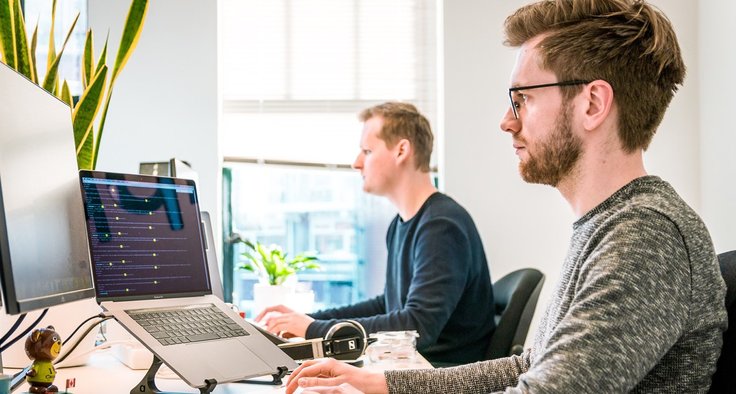 Zwei Personen sitzen vor ihren Laptops