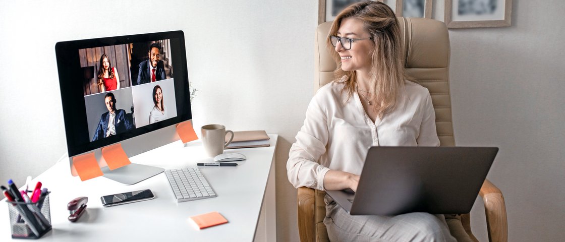 Eine junge Frau sitzt sitzt am Arbeitsplatz und hält eine Videokonferenz